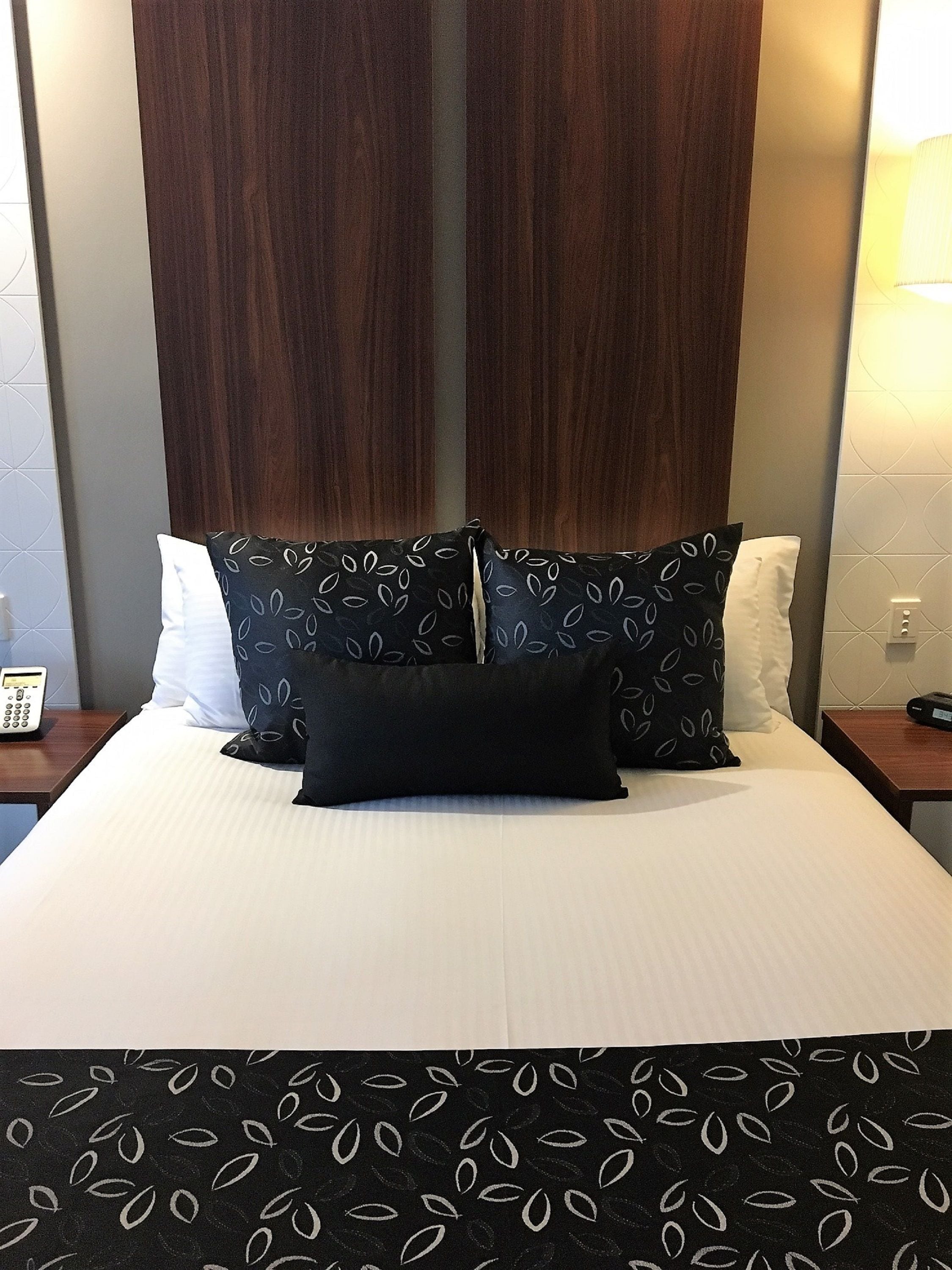 Une chambre d’hôtel avec un grand lit, une tête de lit en bois foncé, des coussins à motifs et une table de chevet avec une lampe.