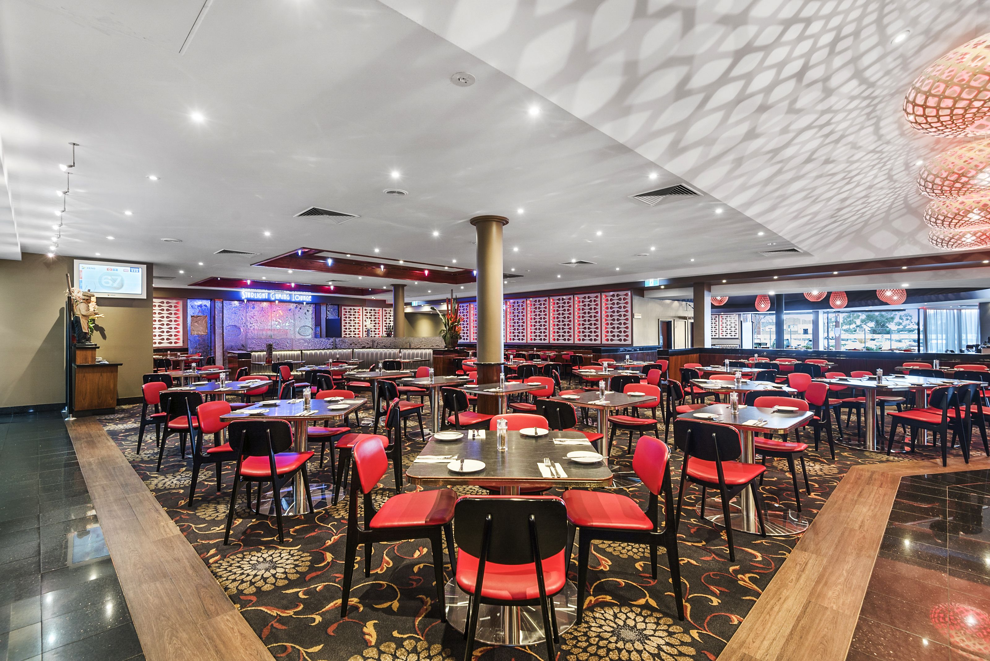 Un restaurante espacioso con varias mesas y sillas, una alfombra estampada y un diseño moderno en el techo.