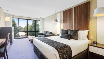 Una habitación de hotel moderna con una cama grande, un escritorio y una zona de estar con vistas al exterior.