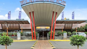 La entrada al Taylors Lakes Family Hotel, con un corredor cubierto, pilares rojos y un letrero que indica un estacionamiento.