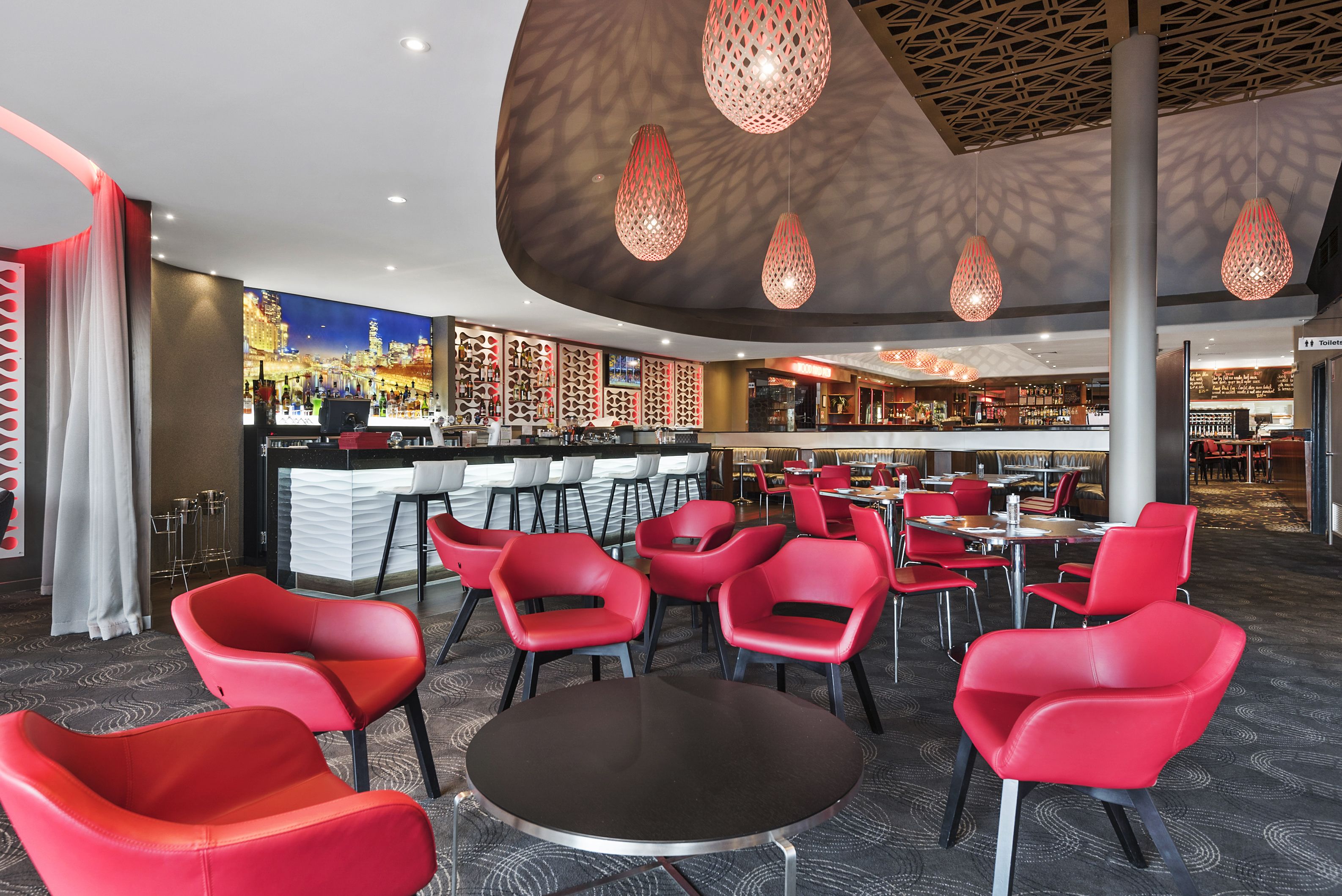 A modern restaurant with red chairs and tables, a bar area, and a cityscape mural on the wall.