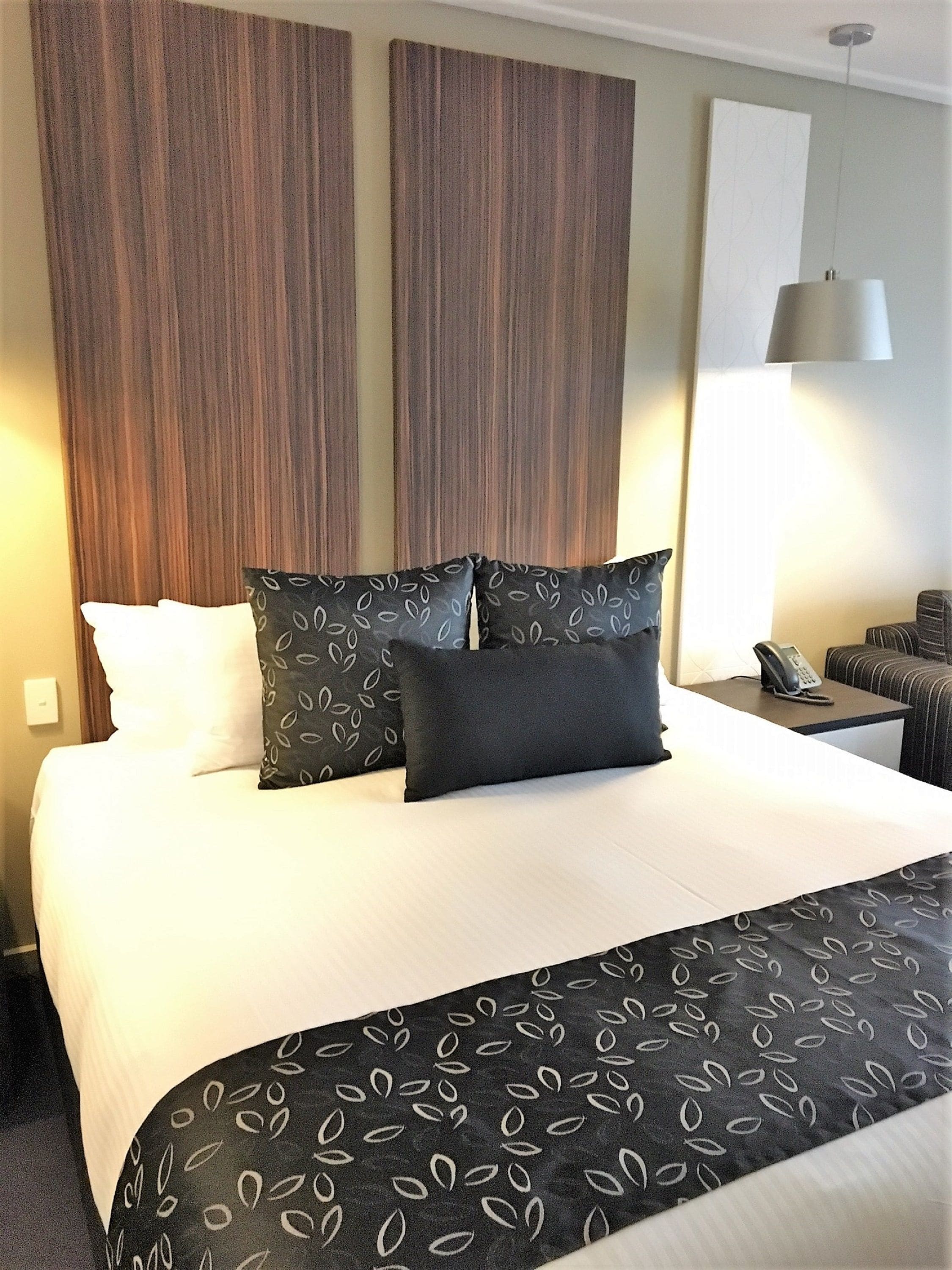 Een hotelkamer met een groot bed, twee kussens, een nachtkastje met telefoon en een lamp.