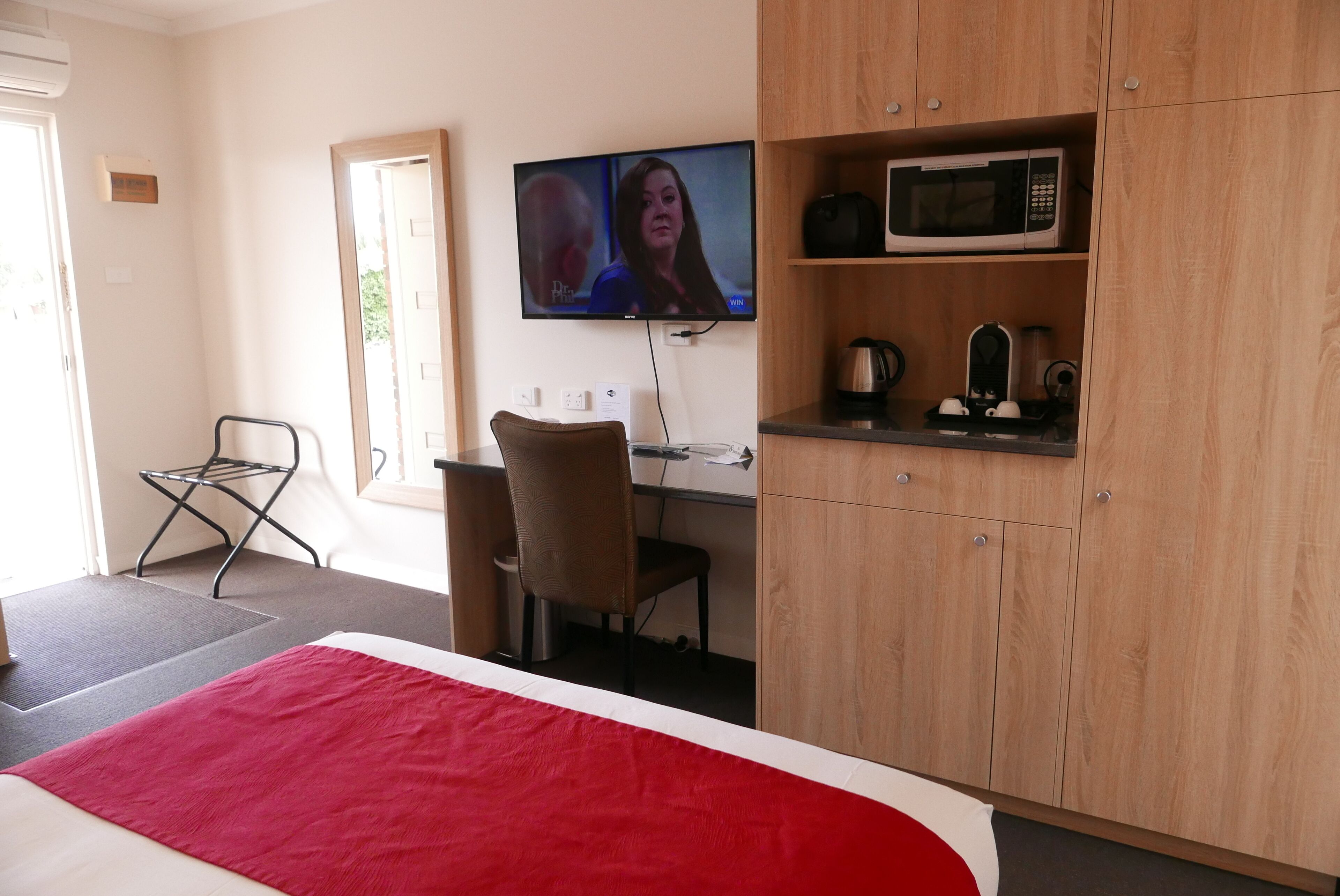 A hotel room with a bed, a desk, a chair, a television, and a microwave.