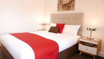 A neatly made bed with a red and white bedspread, a brown headboard, and two bedside tables with lamps.
