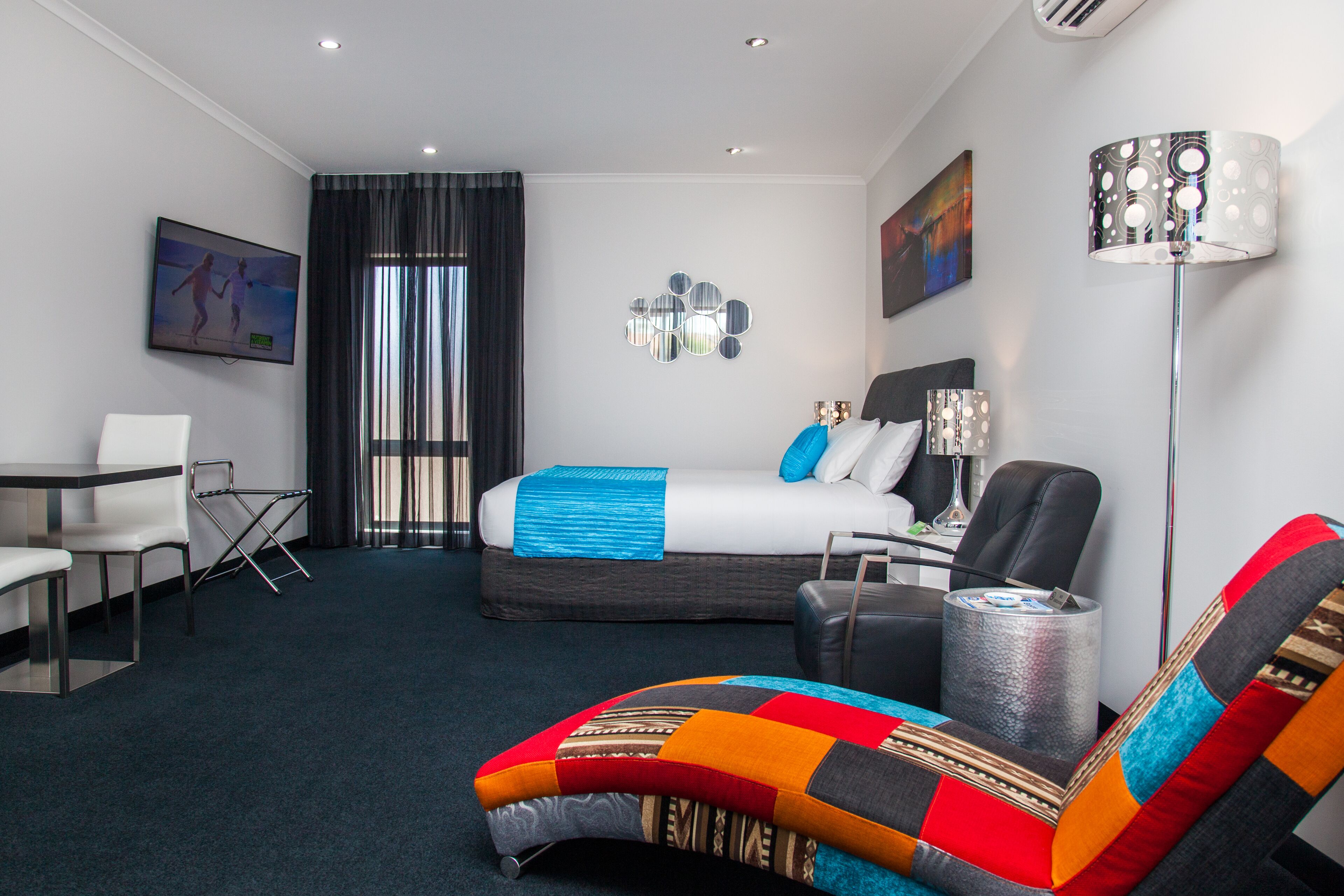 Quarto de hotel com cama, escrivaninha, cadeira, sofá e abajur.