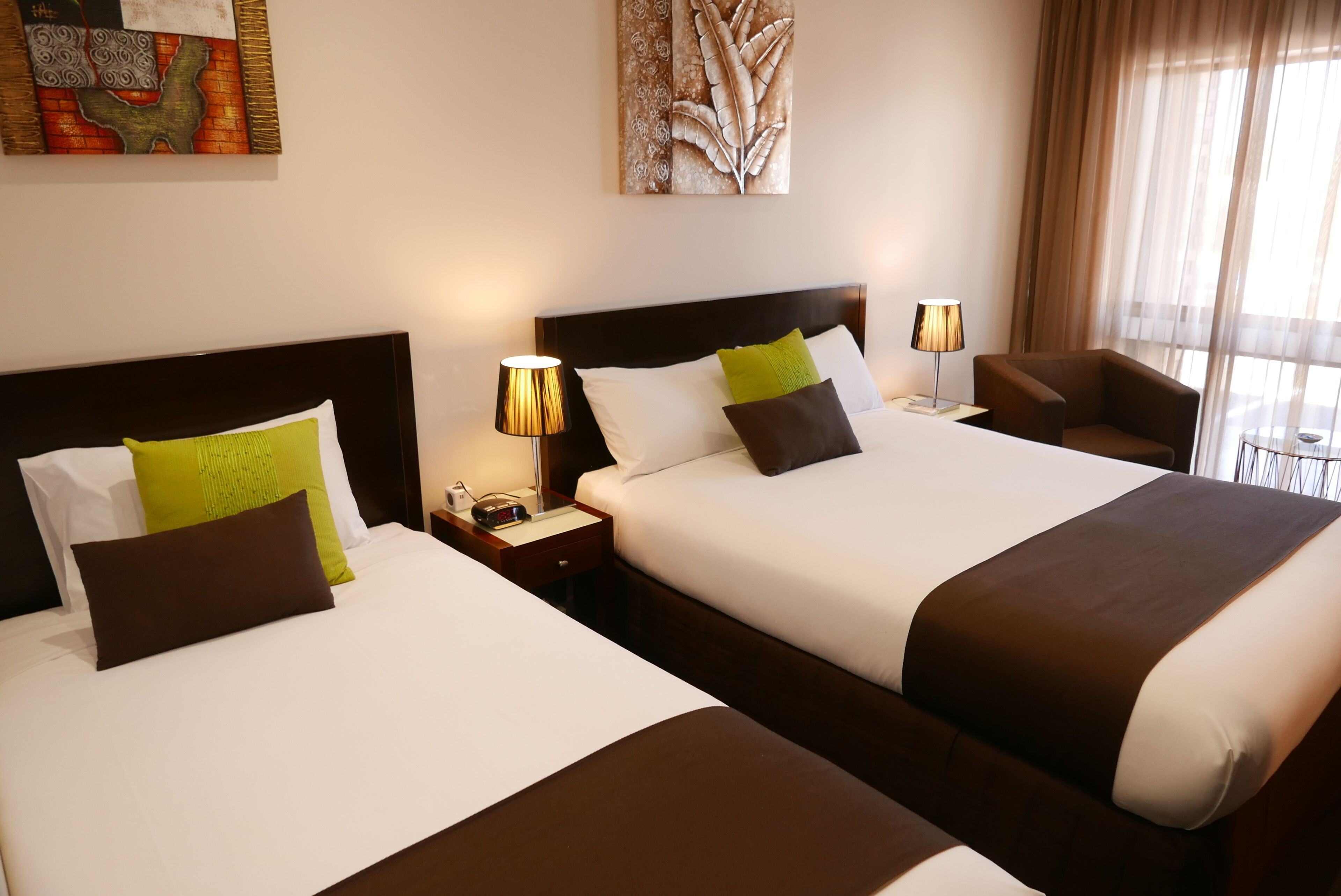 Una habitación de hotel con dos camas, cada una con una mesita de noche, una lámpara y una silla.