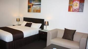 Habitación de hotel con cama, sofá y dos cuadros en la pared.