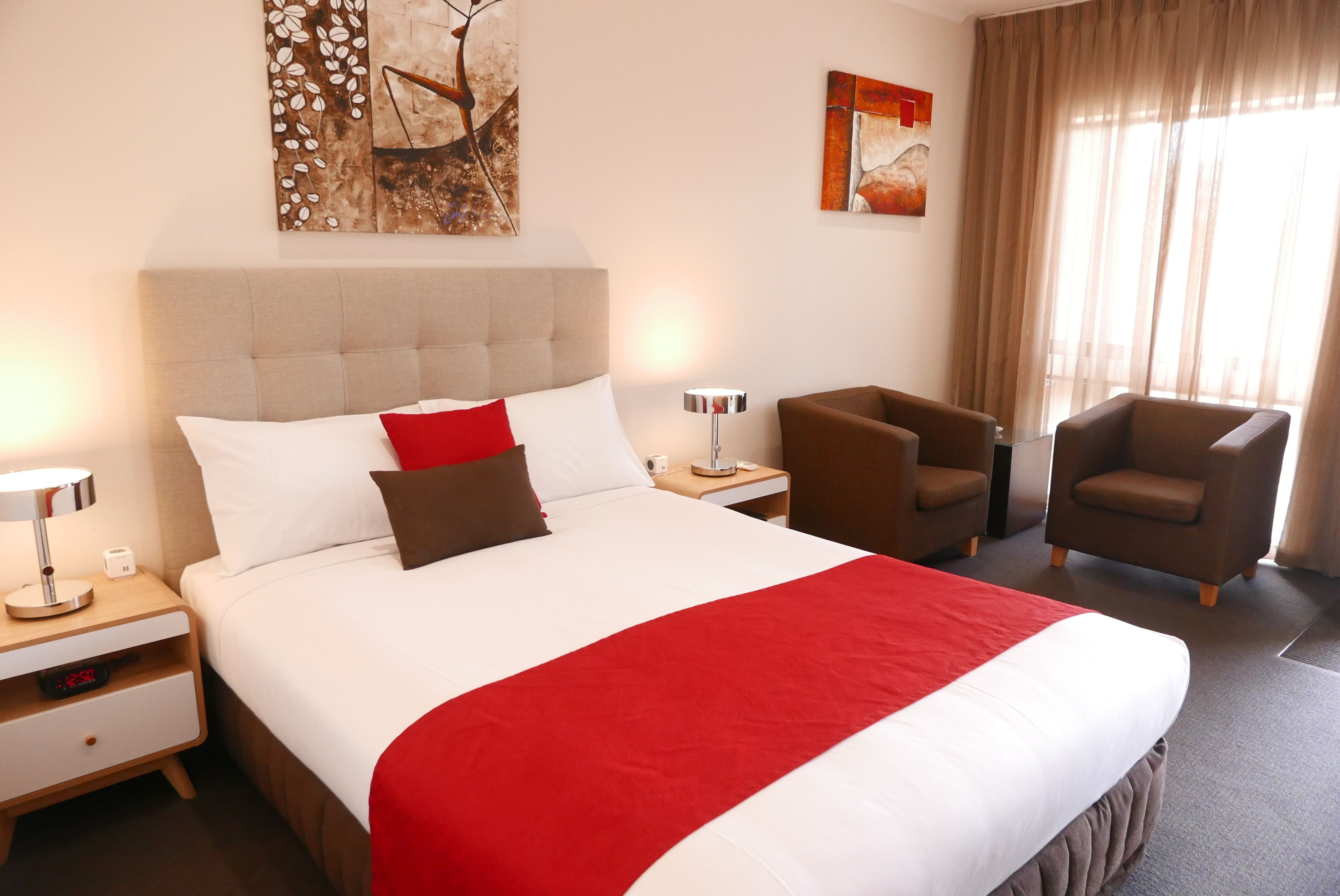 A hotel room with a large bed, two nightstands, a desk, a chair, and artwork on the walls.