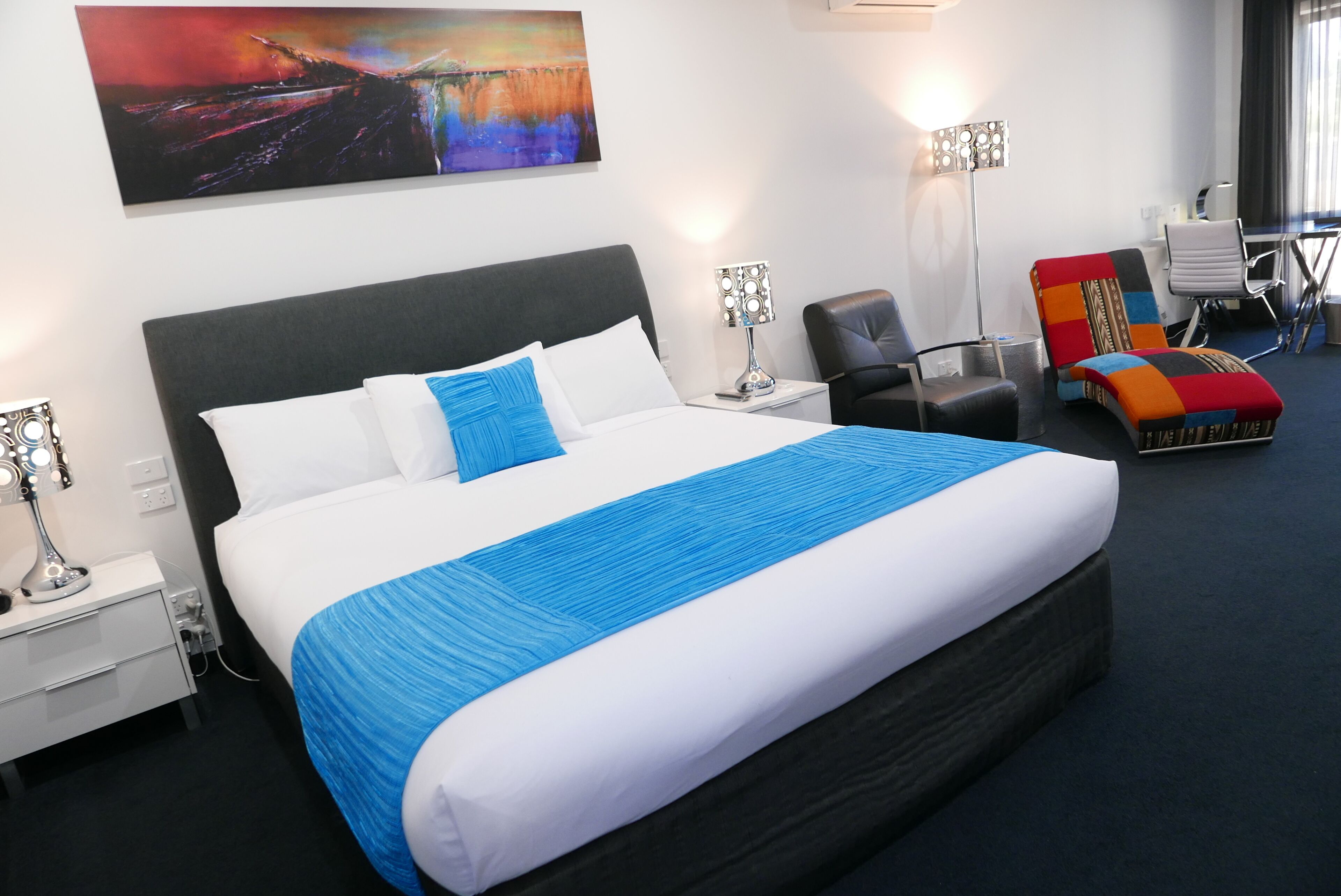 Een hotelkamer met een groot bed, een bureau, een stoel en een schilderij aan de muur.