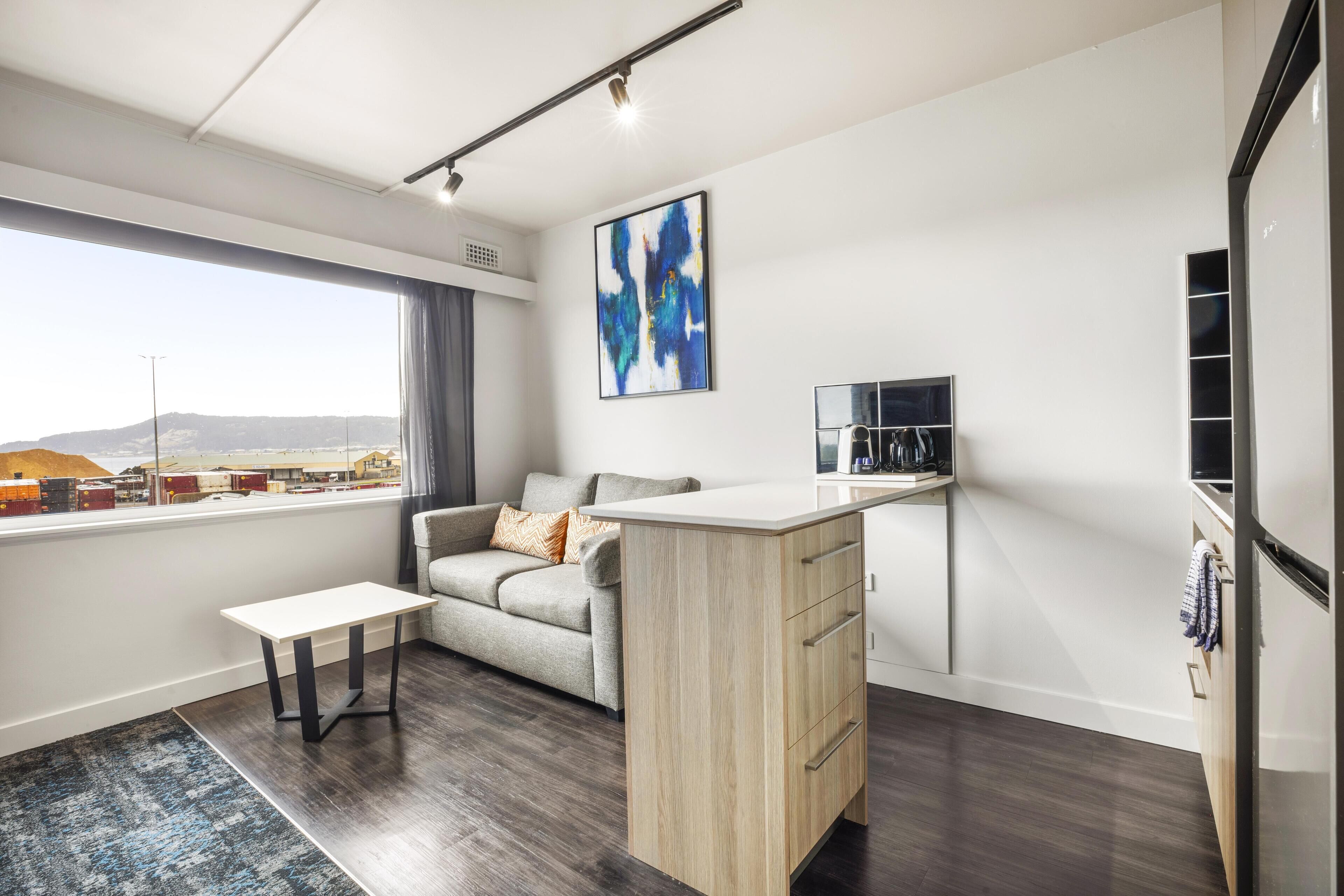 Una sala de estar moderna con un sofá, una mesita, una zona de cocina con mostrador y un ventanal con vistas a la ciudad.