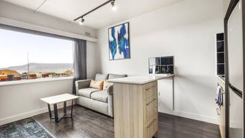 Una sala de estar moderna con un sofá, una mesita, una zona de cocina con mostrador y un ventanal con vistas a la ciudad.