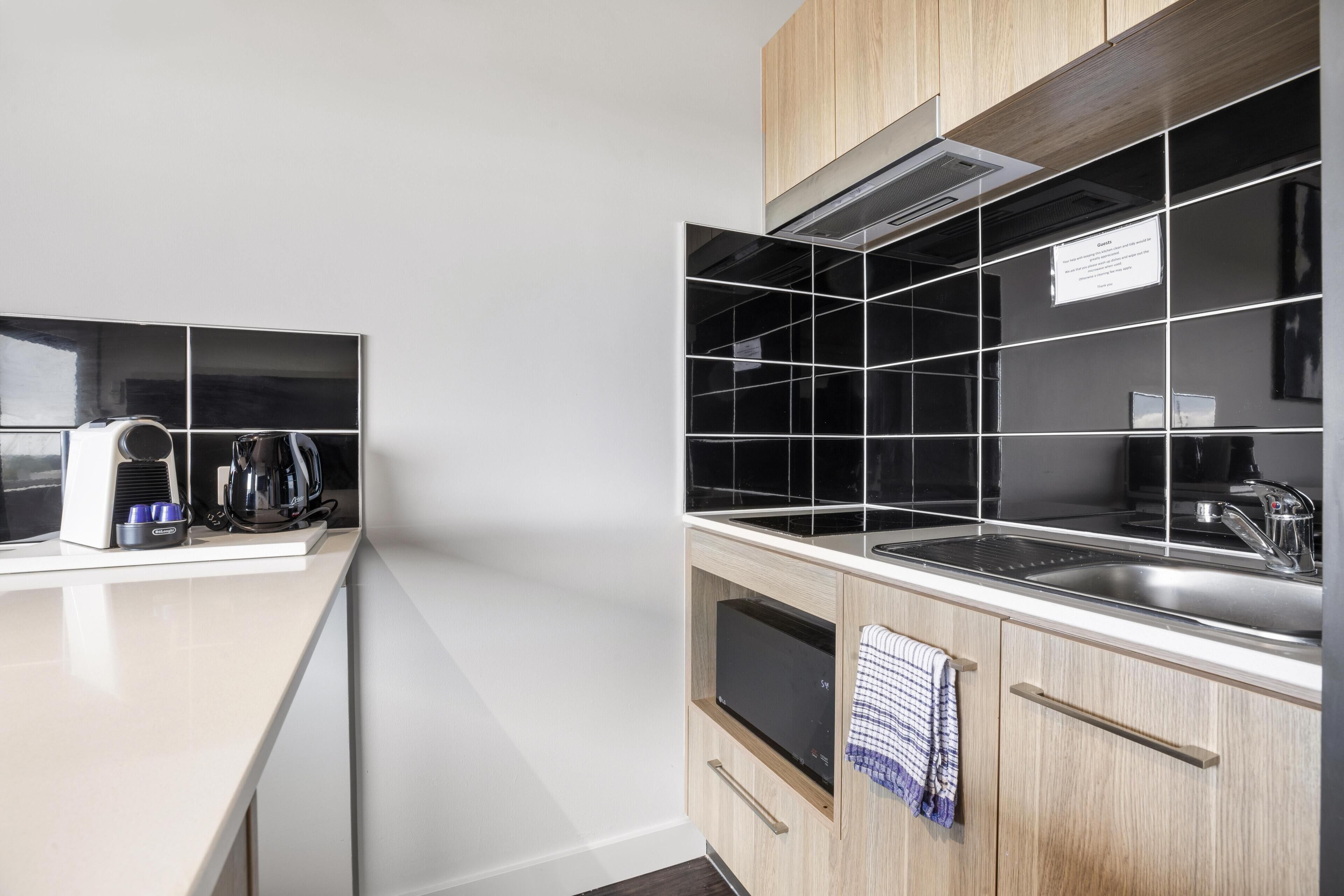 A modern kitchen with a white countertop, black tiled backsplash, and wooden cabinets.