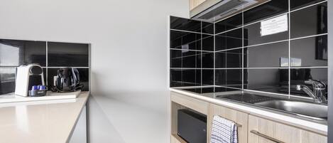 A modern kitchen with a white countertop, black tiled backsplash, and wooden cabinets.