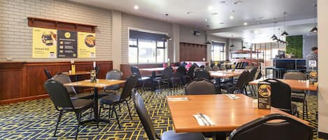 A restaurant with tables and chairs, a patterned carpet, and a brick wall.
