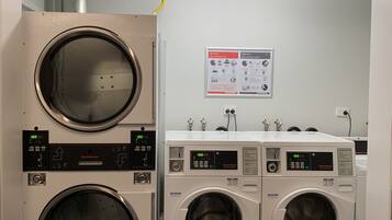 Une laverie équipée de plusieurs machines à laver et de plusieurs séchoirs, une enseigne au-dessus indiquant « Harold Ives », et une affiche avec des instructions de lavage accrochée au mur.
