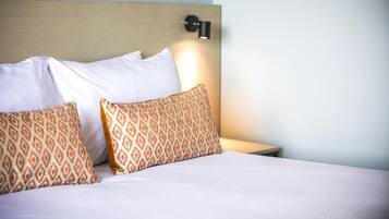A neatly made bed with white and patterned pillows, a wooden headboard, and a wall-mounted light fixture.