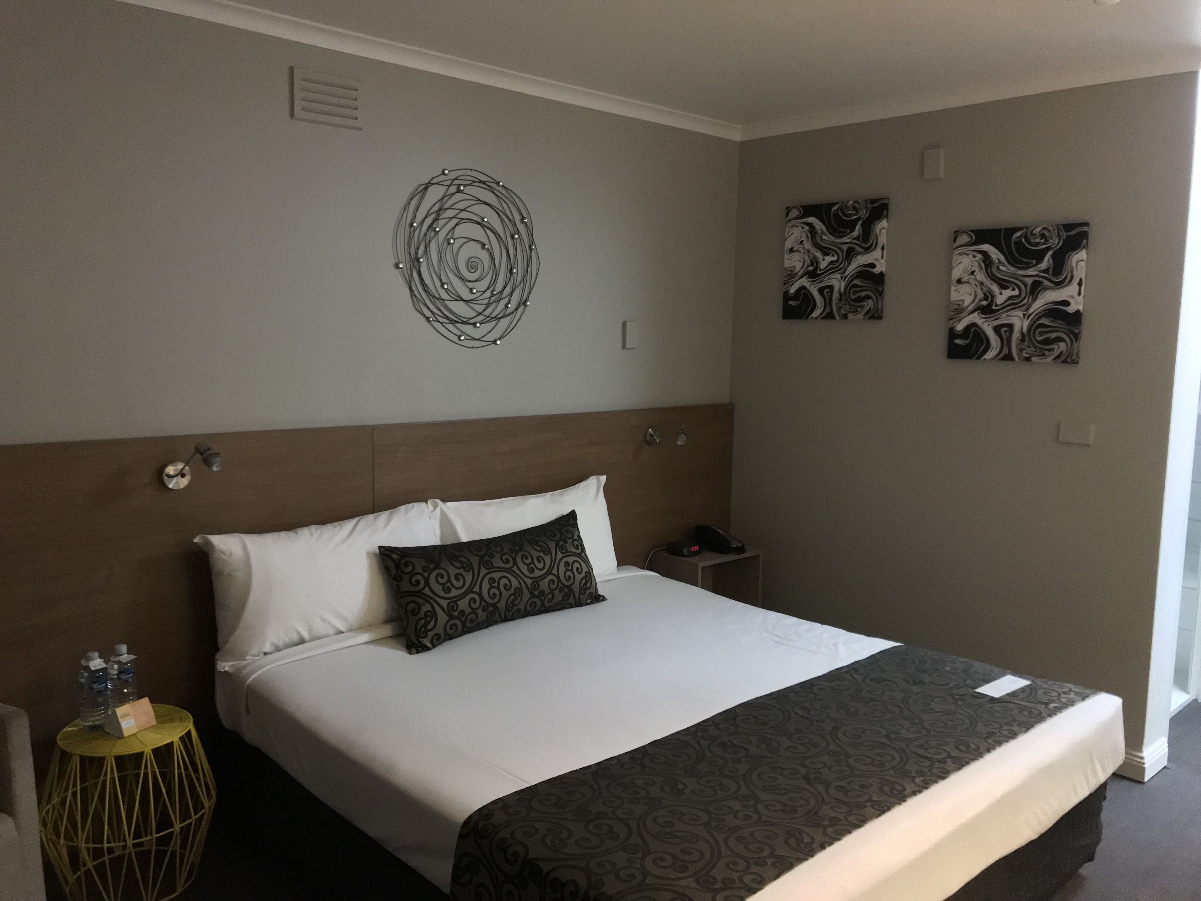 Une chambre d’hôtel comprenant un lit, une table de chevet, une œuvre d’art murale et un luminaire fixé au mur.
