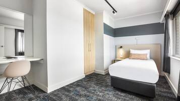 A hotel room with a bed, a desk, a chair, a wardrobe, and a window.