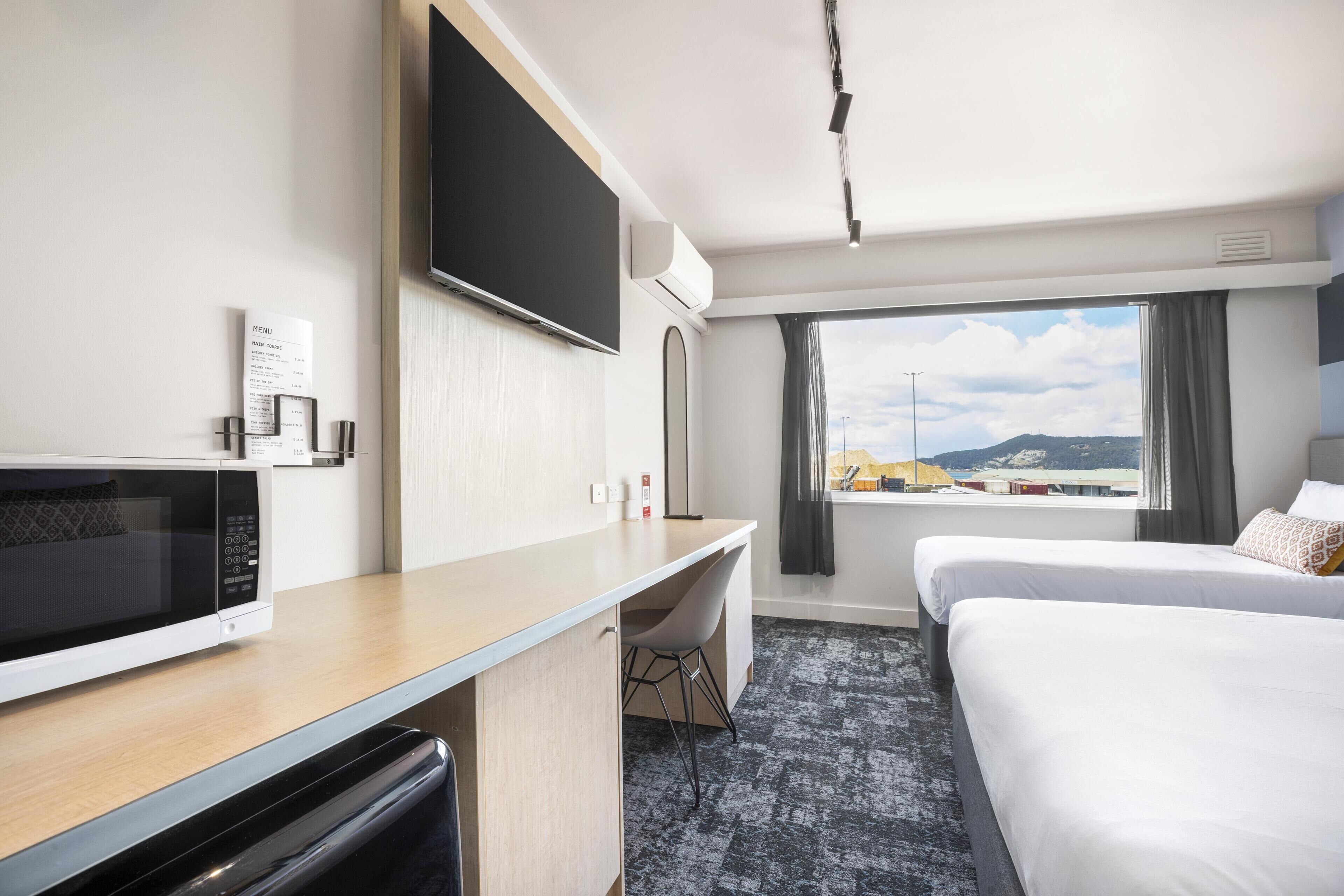 Ein Hotelzimmer mit Bett, Schreibtisch mit Mikrowelle, Fernseher und Fenster mit Blick auf die Stadt.