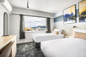 Habitación de hotel con dos camas, un escritorio, una ventana con cortinas y una obra de arte en la pared.