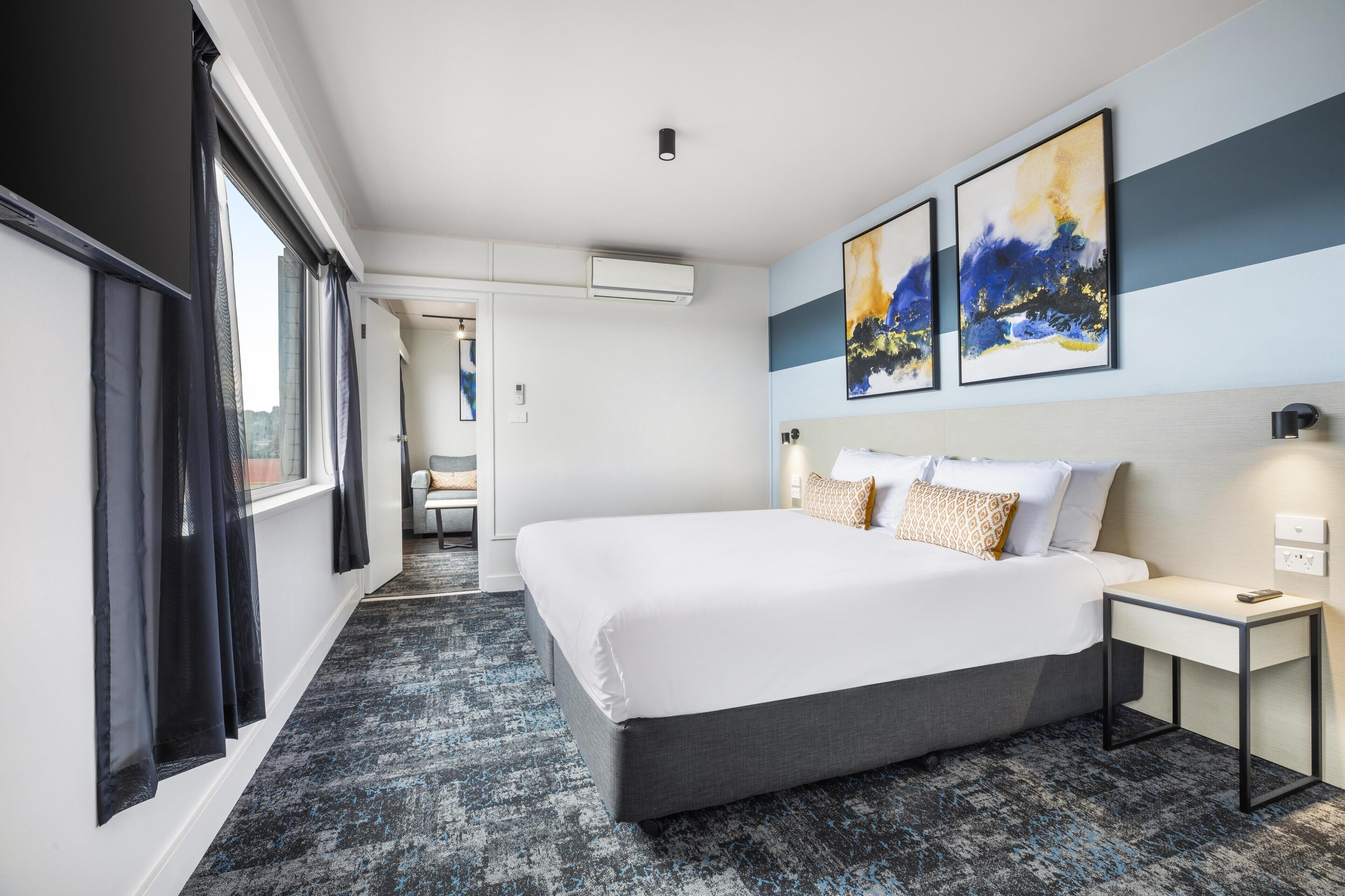 A modern hotel room with a large bed, a bedside table, and artwork on the wall.