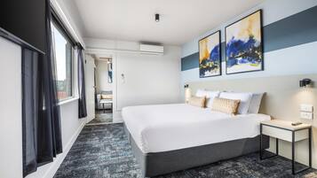 A modern hotel room with a large bed, a bedside table, and artwork on the wall.