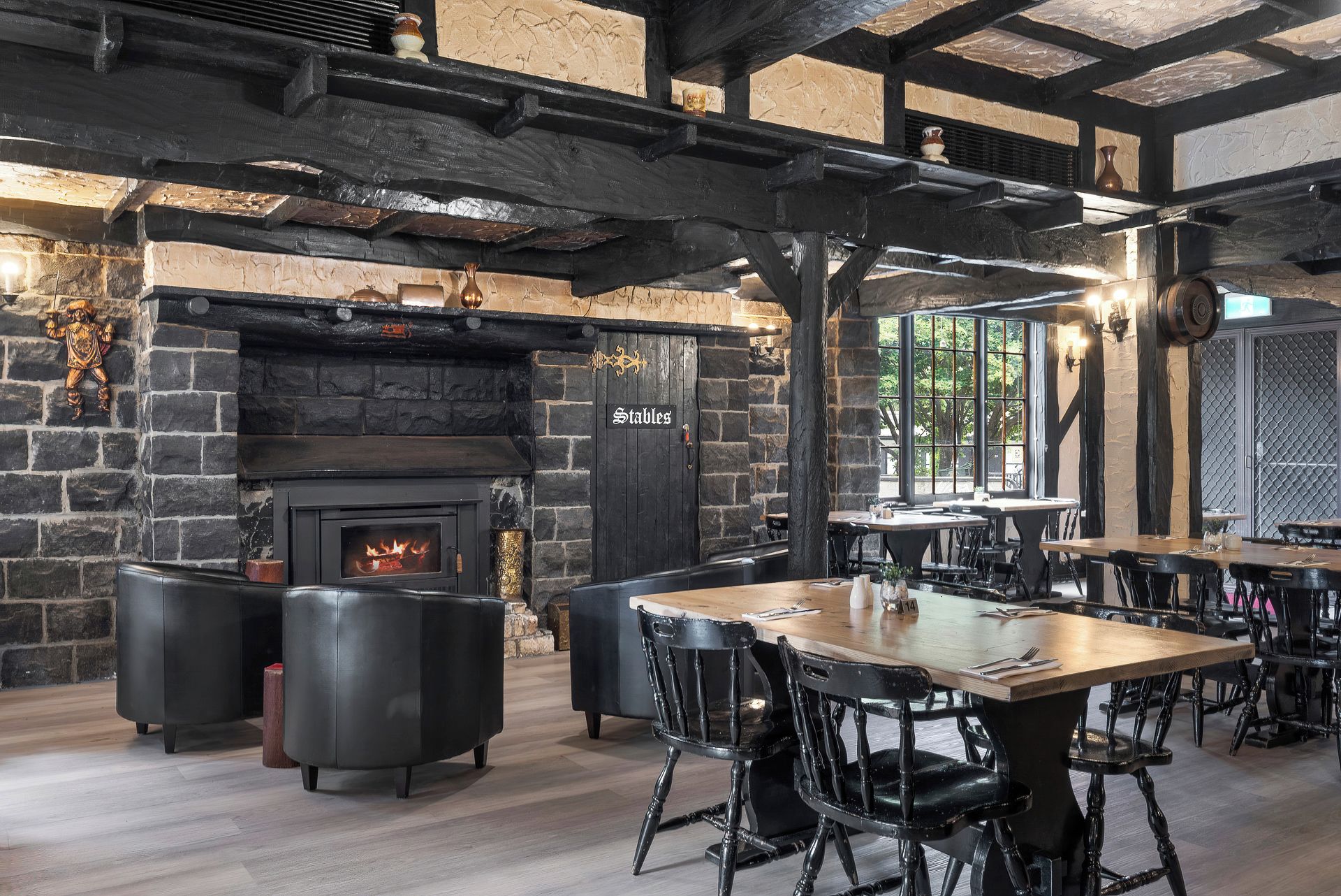 A rustic interior with a stone fireplace, wooden beams, and black leather seating.
