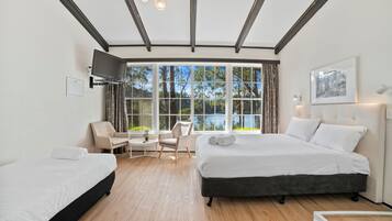 A hotel room with a large bed, a smaller bed, a desk, and a chair. There is a TV mounted on the wall and a window with curtains.