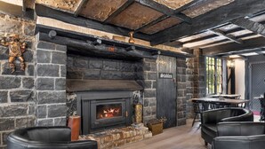 Una chimenea de piedra con fuego, sillones de cuero negro, una mesa de madera y un letrero que dice "Stables".