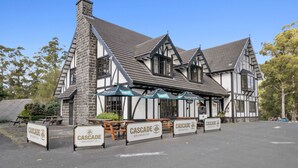 Un edificio de piedra tradicional con techo empinado y estructura de madera, que ofrece asientos al aire libre y señalización para Cascade Brewery Co.
