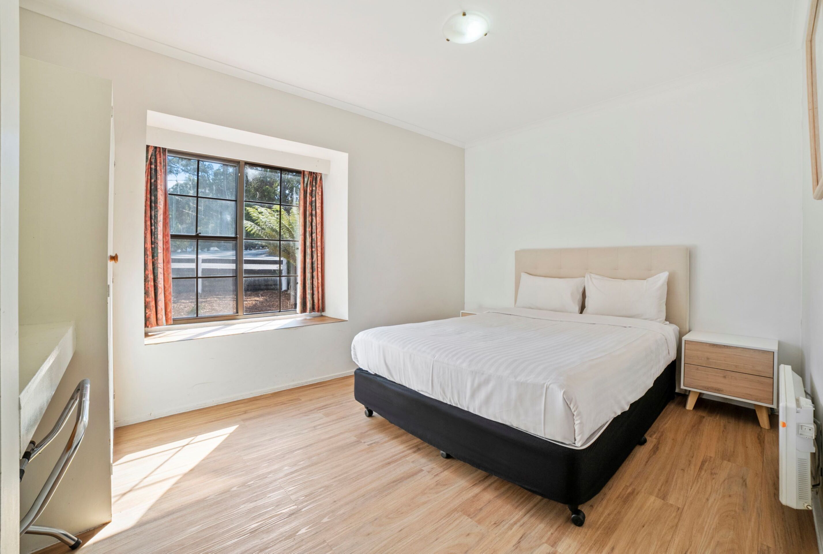 A bedroom with a large bed, a bedside table, a window with curtains, and a radiator.