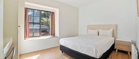 A bedroom with a large bed, a bedside table, a window with curtains, and a radiator.