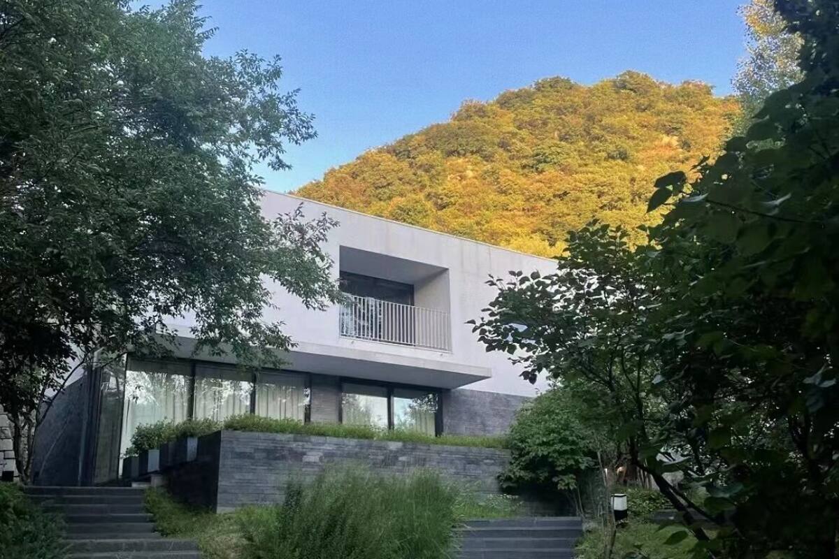 A modern house with a balcony, surrounded by trees and a hillside.