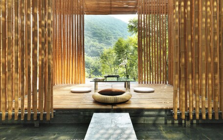 A room with a wooden deck, a stone bench, and a view of a forested mountain.