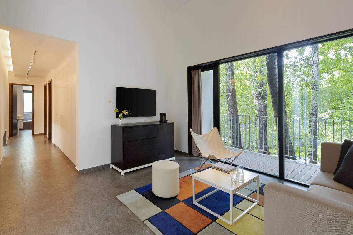 A modern living room with a large window, a flat-screen TV, a sofa, a coffee table, and a chair.