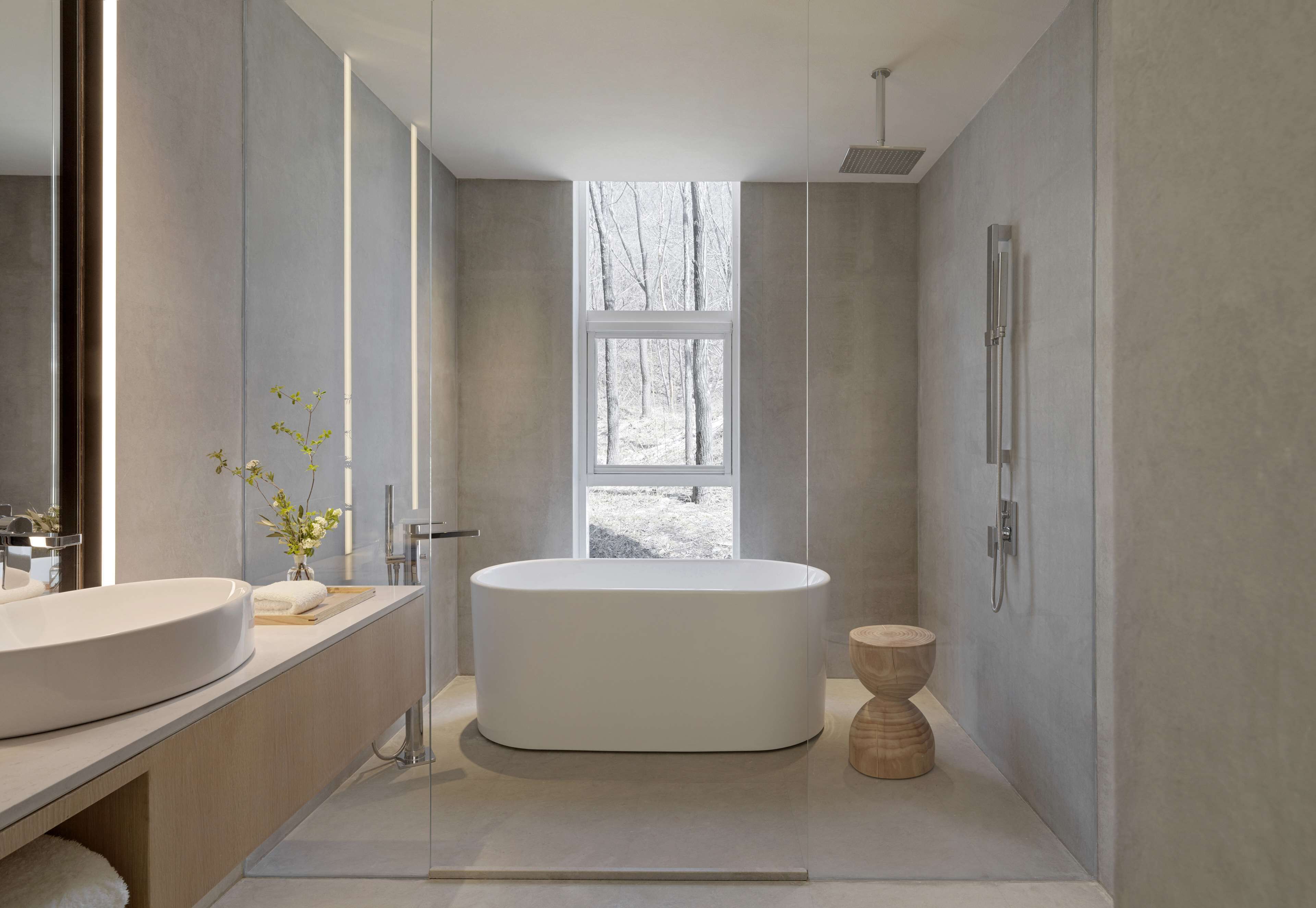 Une salle de bain moderne avec une baignoire sur pieds, un grand miroir et une fenêtre donnant sur un paysage enneigé.