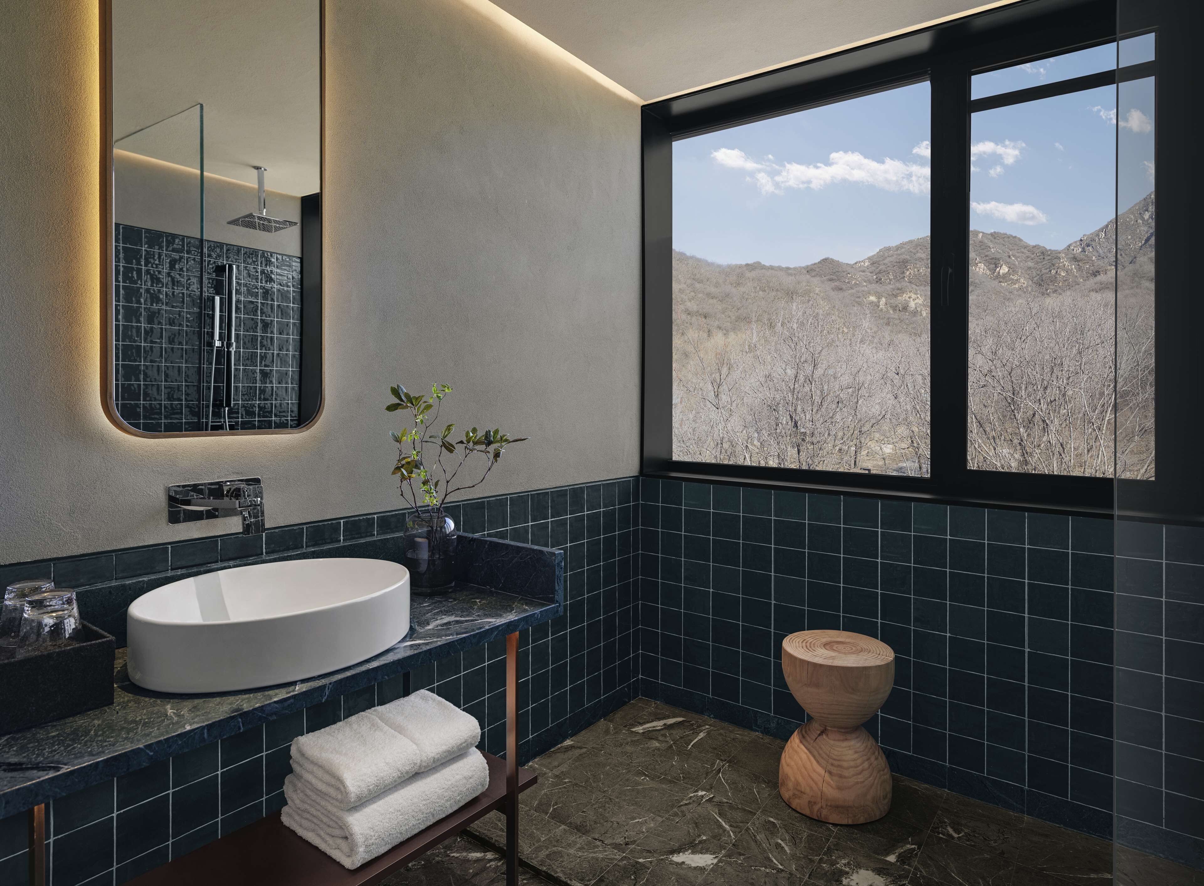 A bathroom with a large window, a sink, a mirror, and a wooden stool.