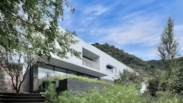Una casa moderna con balcón, rodeada de abundante vegetación y cielo despejado.