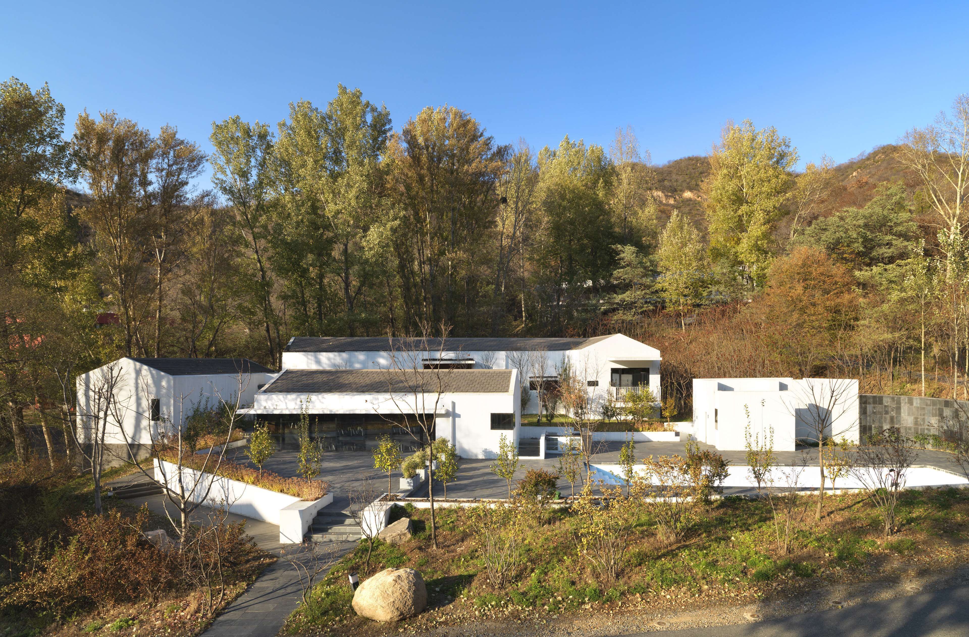 Una casa moderna con techo plano, rodeada por un paisaje natural con árboles y colinas.