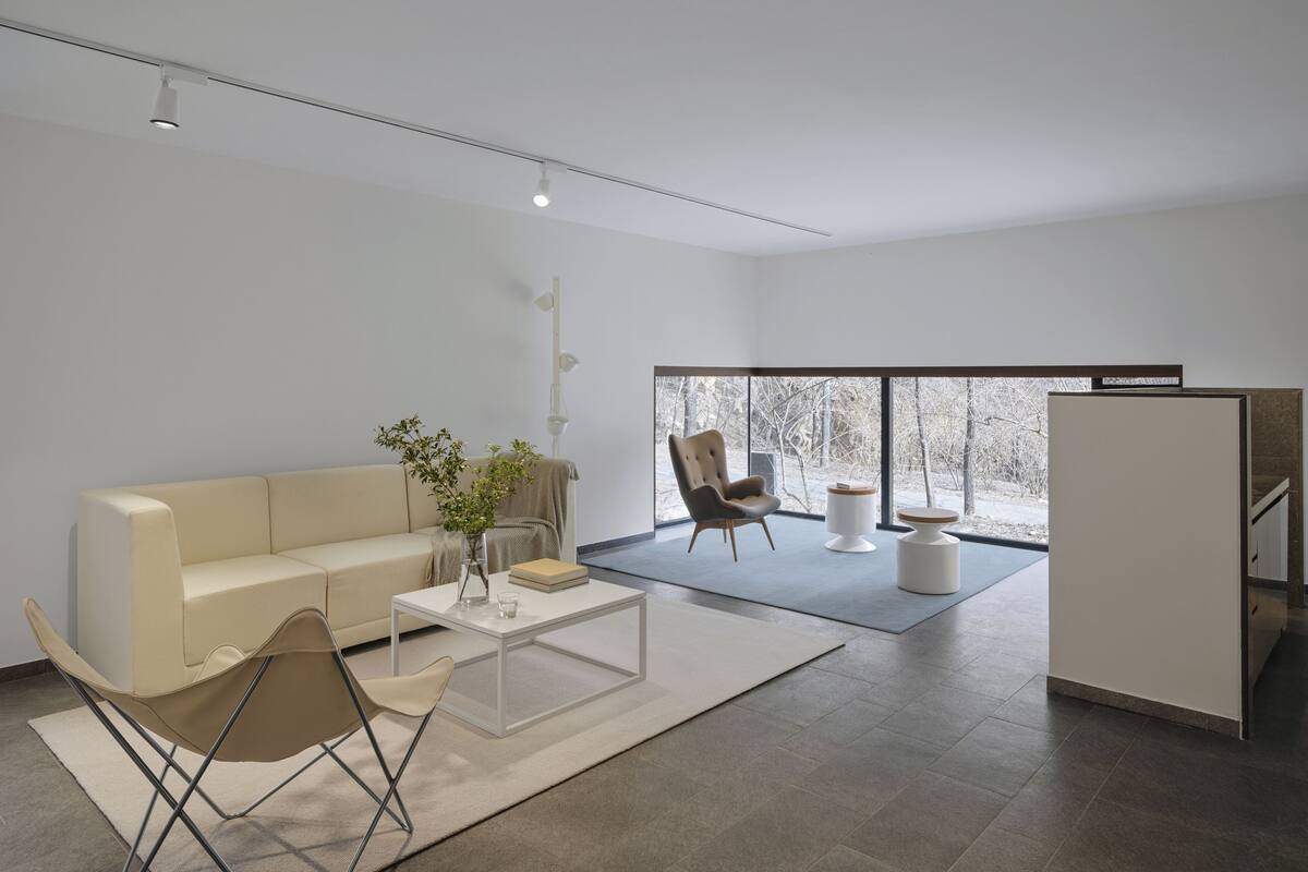 A modern living room with a sofa, coffee table, and chairs, a large window with a view of trees, and a minimalist design.