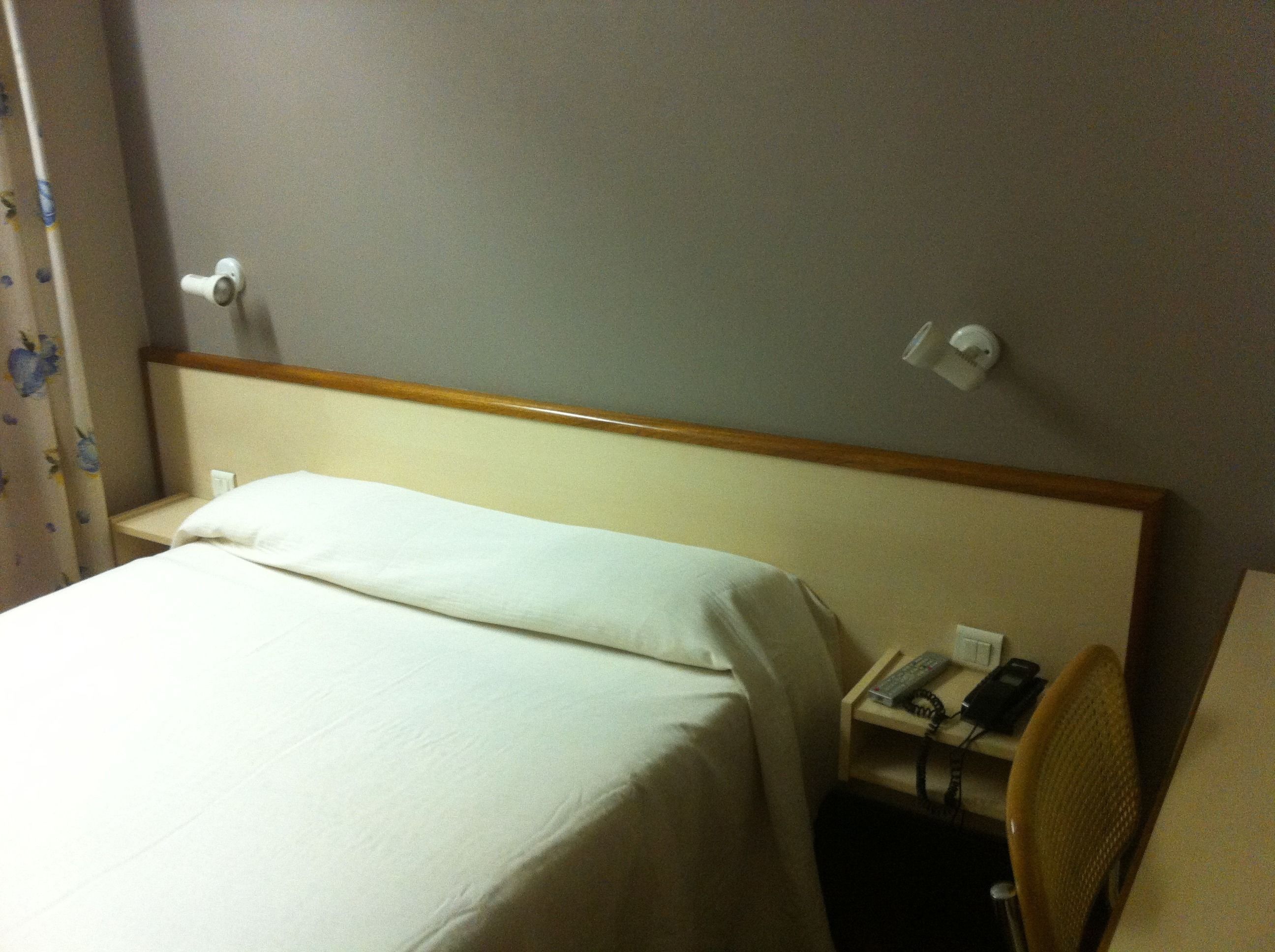 A hotel room with a bed, a nightstand with a phone, and a chair.