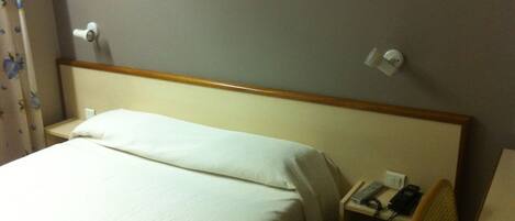 A hotel room with a bed, a nightstand with a phone, and a chair.