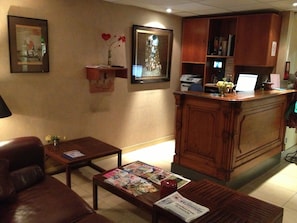 A lobby with a reception desk, a leather sofa, a coffee table with magazines, and a wall with framed artwork and a vase with flowers.
