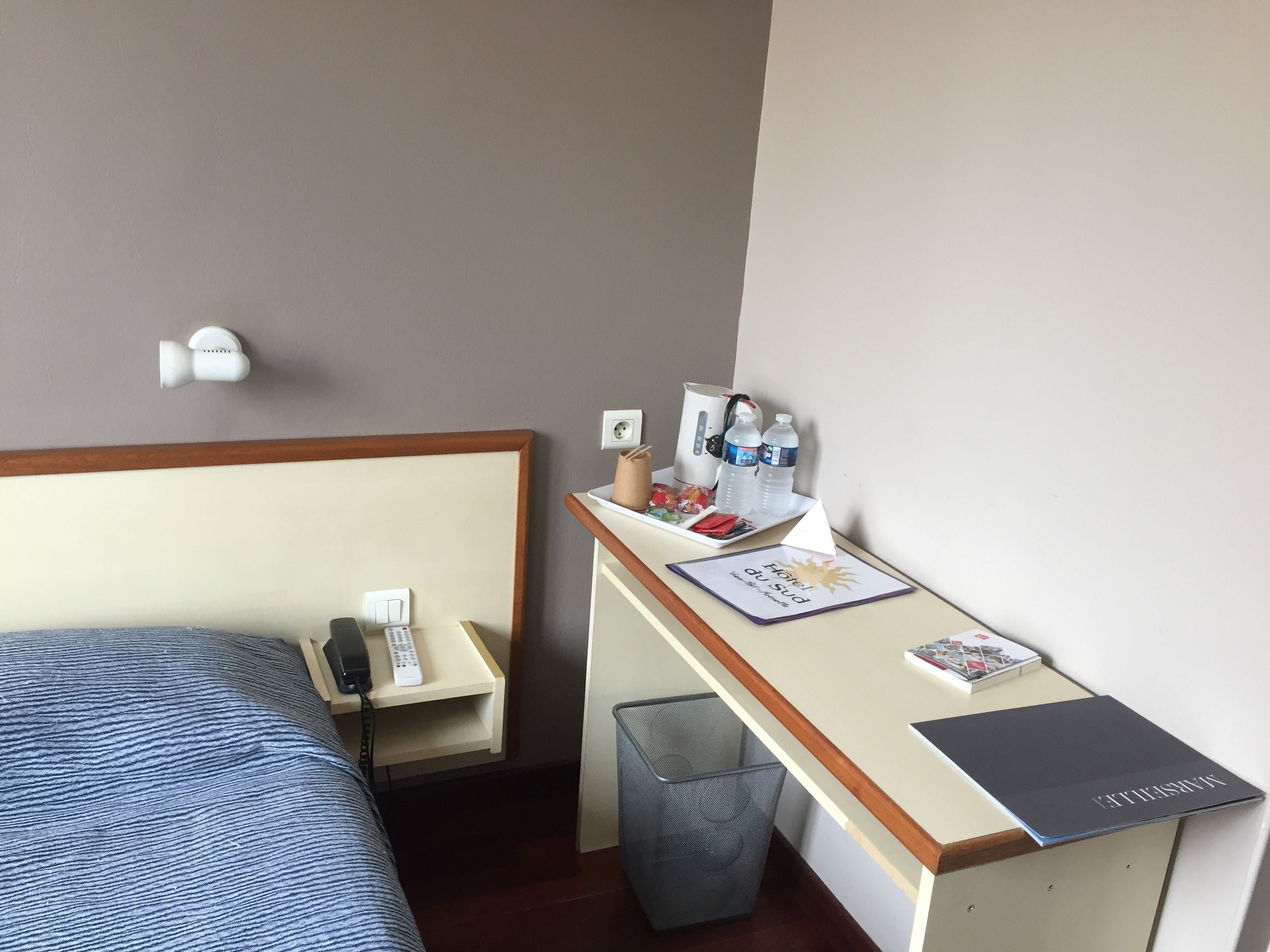 Une chambre d’hôtel comprenant un lit, un bureau avec un ordinateur portable, une poubelle et une petite table avec des articles de toilette.