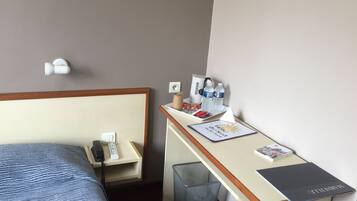 Une chambre d’hôtel comprenant un lit, un bureau avec un ordinateur portable, une poubelle et une petite table avec des articles de toilette.