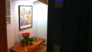 Ein Flur mit einem gerahmten Kunstwerk, einem Holztisch mit roten Blumen und einer digitalen Anzeige, die die Zahl 44 zeigt.