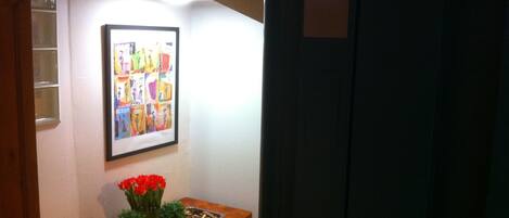 A hallway with a framed artwork, a wooden table with red flowers, and a digital display showing the number 44.