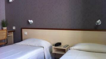 A hotel room with two single beds, a bedside table with a phone, and a small shelf.