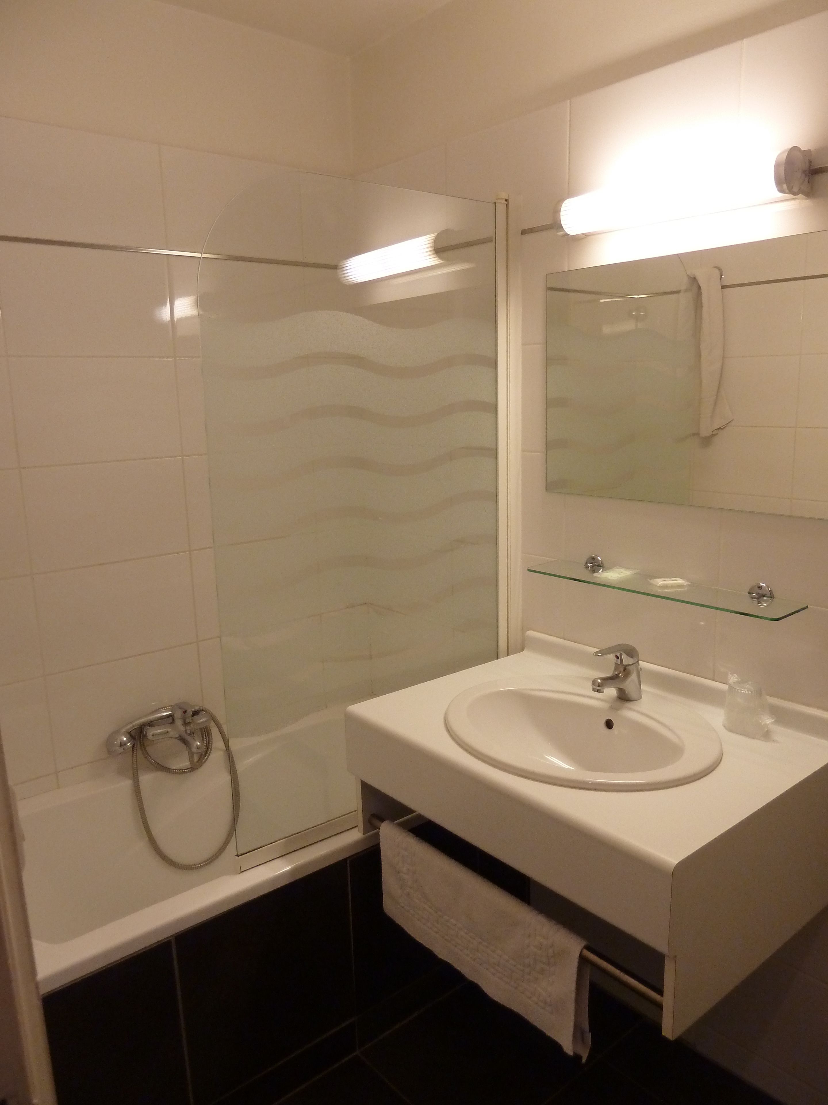 A modern bathroom with a glass shower enclosure, a white sink with a mirror above it, and a glass shelf.