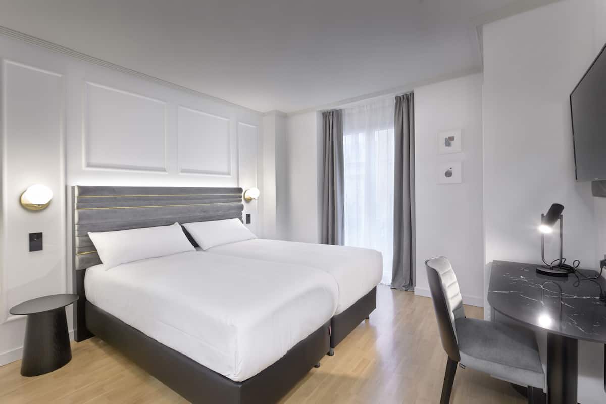 A modern hotel room with a large bed, a desk with a chair, and a flat-screen TV.